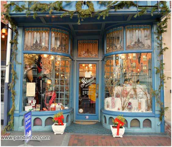 عکس مغازه شیرینی فروشی با در ورودی چوبی جالب و دکوراسیون خاص. در تصویر گلها و گلدان های زیبا در کنار درب چوبی مغازه و دکان وجود دارد