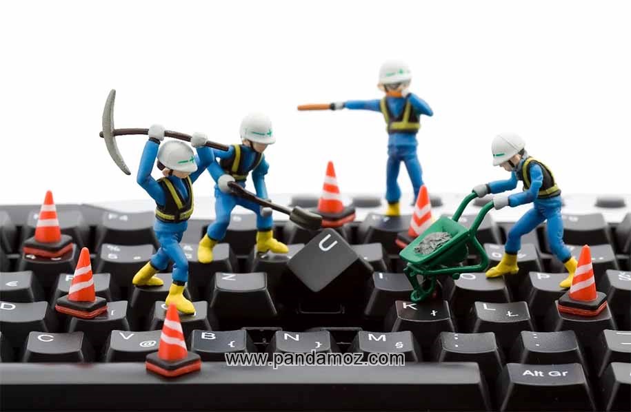 عکس نقاشی فانتزی از کیبورد کامپیوتر که تعدادی مهندس کامپیوتر با لباسهایی مشابه لباس کارگران ساختمانی روی کی بورد و با بیل و کلنگ و فرگون در حال ریختن ملات و تعمیر کلیدها هستند