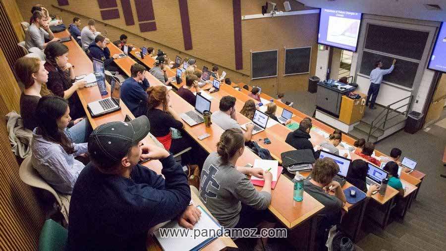عکس کلاس درس عمومی در تالار دانشگاه و کلاس به صورت پله ای و دانشجویانی که در نیمکت های خود نشسته اند و استاد درس می دهد