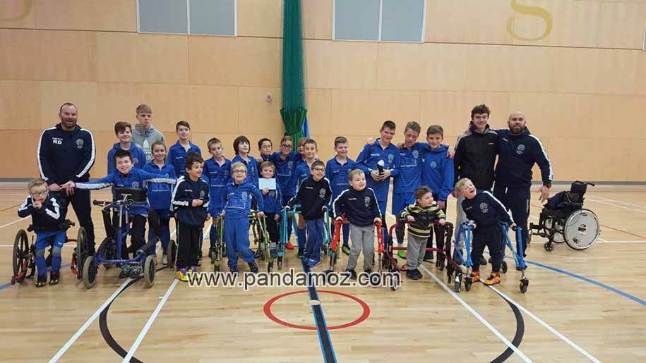 عکس دسته جمعی تیم فوتبال و مربیان و دانش آموزان مدرسه معلولان ناتوان و استثنایی. تصویر بچه ها در سالن سرپوشیده با وسائل بازی است