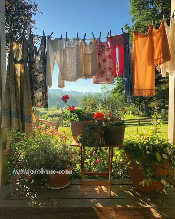 عکس بسیار زیبا از لباس ها و رختهای آویزان شده روی بند و طناب. در تصویر منظره زیبای کوهستان از دوردست و فضای سرسبز، درختان، گلها، گیاهان، چمنزار بسیار قشنگ دیده می شوند