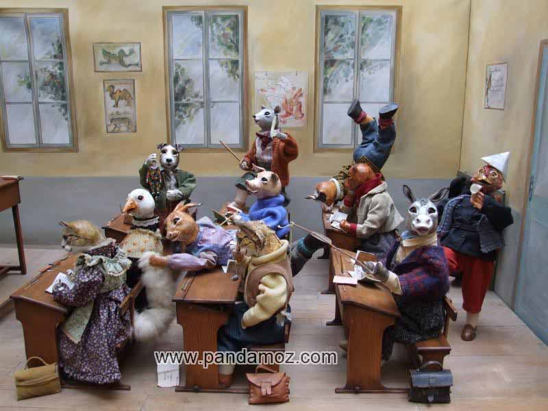 عکس نمایش عروسکی از مدرسه حیوانات و کلاس درس حیوانات. در تصویر حیوان های مختلف پشت نیمکت های کلاس درس نشسته اند و هر حیوانی رفتار و بازیگوشی خاصی دارد. انواع بچه های حیوانات در کلاس حضور دارند