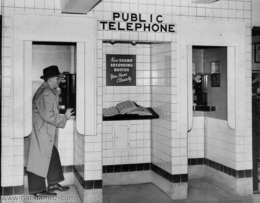 عکس یک مرد که با تلفن عمومی و همگانی به صورت ایستاده در حال مکالمه است.در تصویر سه محل جداز هم هم برای تلفن کردن دیده می شود. مرد لباس بلند و پالتو با کلاه لبه دار پوشیده