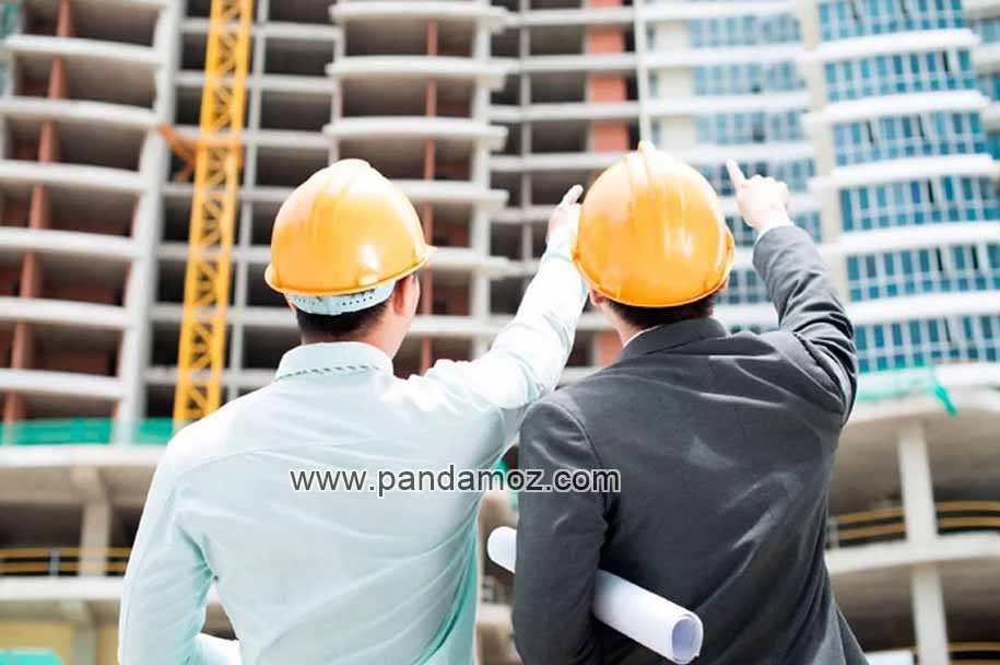 عکس دو مهندس ساختمان که در پایین برج های در حال ساخت ایستاده اند و به بالای برج ها اشاره می کنند. در تصویر هر دوی مهندسهای ناظر و مجری ساخت ساختمان کلاه ایمنی زرد رنگ بر سر دارند