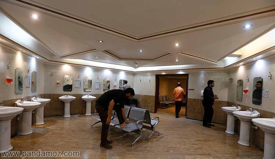 عکس یک وضوخانه مدرن و تمیز مسجدی در تهران در تصویر یک مردی پس از وضو گرفتن پای خود را روی صندلی گذاشته و در حال کشیدن مسح روی پای خود است. فرد دیگری در آینه نگاه می کند