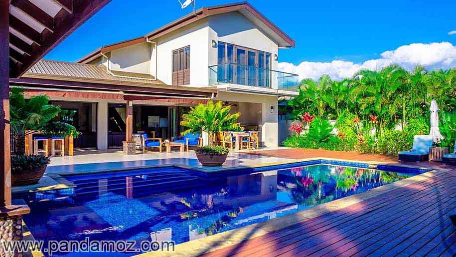 عکس بسیار زیبا از یک کاخ و حیاط دارای استخر رو باز. در تصویر آب استخر آبی و صاف و زلال و عکس ساختمان در آن دیده می شود