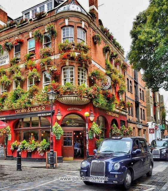 عکس یک رستوران بسیار زیبا در کاونت گاردن در مرکز خرید و سرگرمی در غرب لندن انگستان و محل استقرار فروشگاه ها و غرفه ها و دکه های صنایع دستی. رستوران چند طبقه که بر روی دیوارهای رنگی و قرمز آن و  کنار پنجره ها گل و گیاه کاشته شده