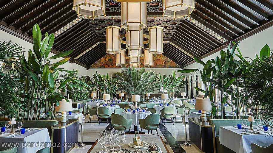 عکس رستوران زیبا با طرحی جالب و جذاب به همراه گلدان های گیاهان سبز و میزها و صندلی های متناسب. در تصویر لوسترهایی نیز از سقف آویزان است