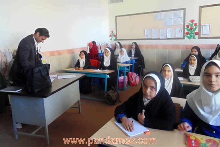 عکس کلاس درس دبیرستان دخترانه با معلم مرد در کلاس. در تصویر کلاس مدرسه، دانش آموزان دختر بر روی صندلی ها نشته اند و آقای معلم پشت میز خودش ایستاده است بعضی ها چادر بر سر دارند